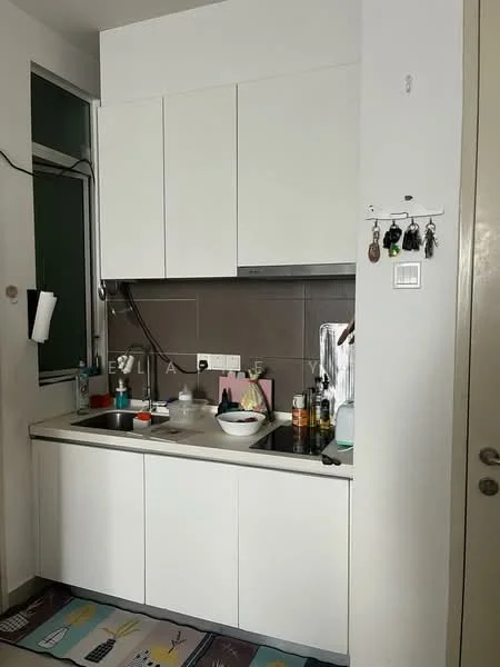 Kitchen features: white cabinetry, grey tiled backsplash, single-bowl stainless-steel sink, chrome pull-down faucet, countertop with integrated cooktop, built-in oven, microwave, kitchen utensils on countertop, wall-mounted hooks for keys, window for natural light, flooring with decorative mat; style: modern.