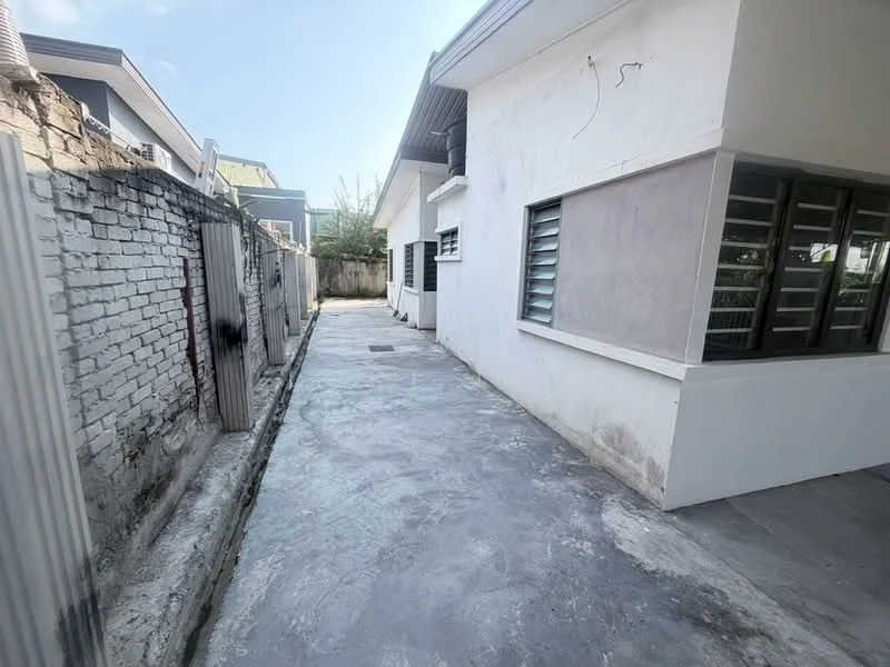Exterior features: white painted facade, concrete flooring, fenced boundary, side walkway, windows with metal grilles, single-storey structure, exposed brick wall, clear sky, adjacent building visible; style: modern.