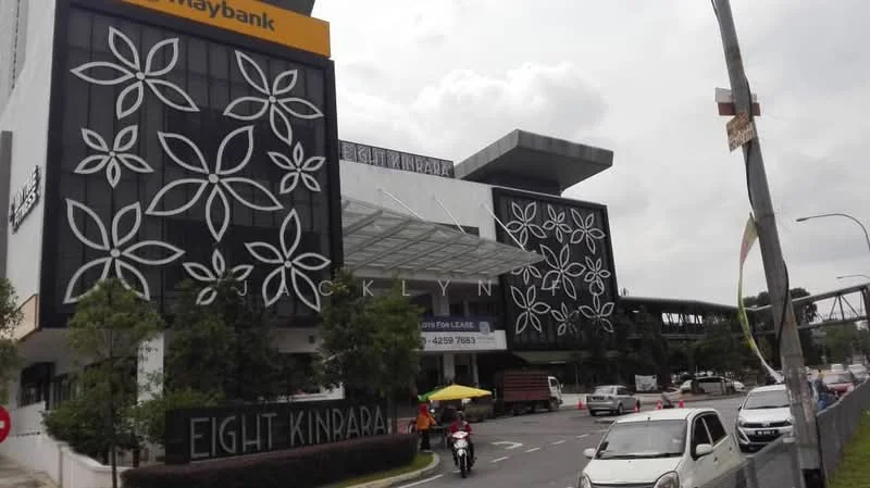 Exterior type: mixed-use development; features: modern facade with floral patterns, glass awning entrance, two-storey structure, signage for Eight Kinrara, Maybank branch visible, surrounding landscaping with trees, road access with vehicles, parking area in front; style: modern.