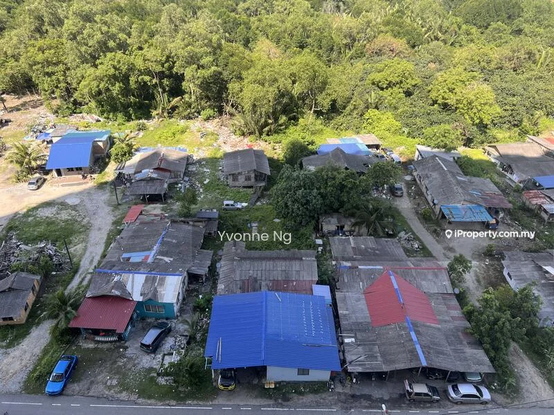Exterior type: low-rise apartment block; features: blue metal roofing, single-storey houses, surrounding greenery, paved road, scattered palm trees, open land with debris, residential area; style: traditional.