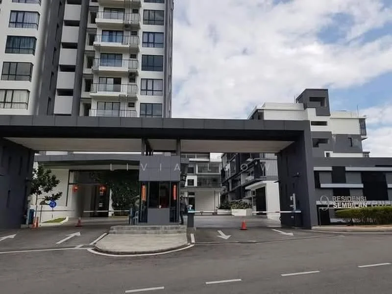 Exterior type: mid-rise condominium; features: modern facade with grey and white elements, covered entrance with awning, landscaped area with small trees, driveway leading to entrance, parking area visible, multiple storeys, glass windows, signage for 'Residensi Semblian', surrounded by open space, urban context with nearby buildings; style: modern.
