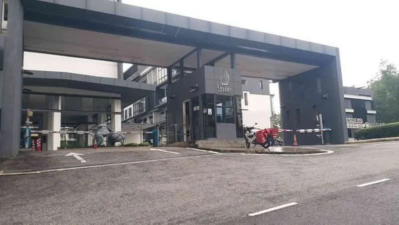 Exterior type: low-rise apartment block; features: modern facade with dark grey cladding, covered entrance with awning, security guardhouse at entrance, parking area with marked bays, landscaped greenery at entrance, bicycle parking area, driveway with interlocking pavers; style: modern.