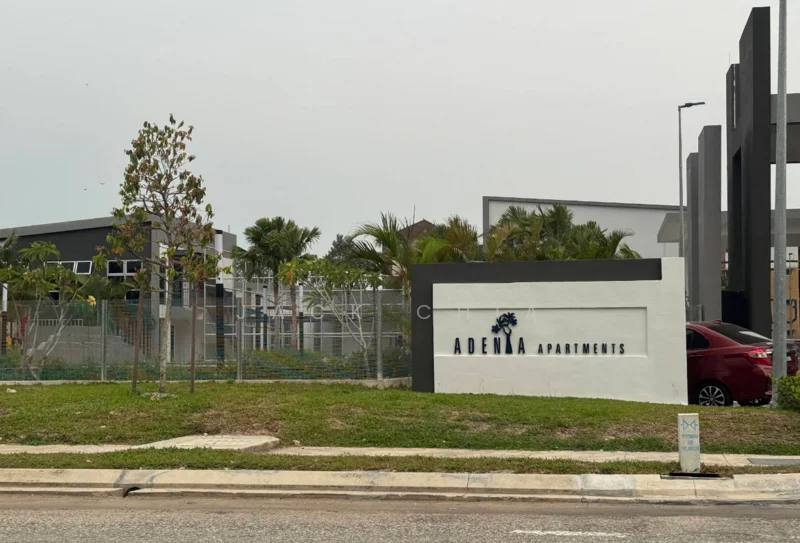 Exterior type: low-rise apartment block; features: signage with 'Adenia Apartments', manicured lawn, landscaping with small trees, surrounding fencing, paved walkway, parking area visible, modern architectural elements; style: modern.