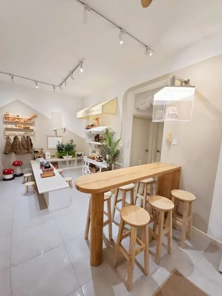 Kitchen features: wooden breakfast bar with stools, white dining table, white chairs, light grey tiled flooring, white walls, shelves with decorative items, green plants, track lighting, recessed ceiling lights, open layout; style: modern.