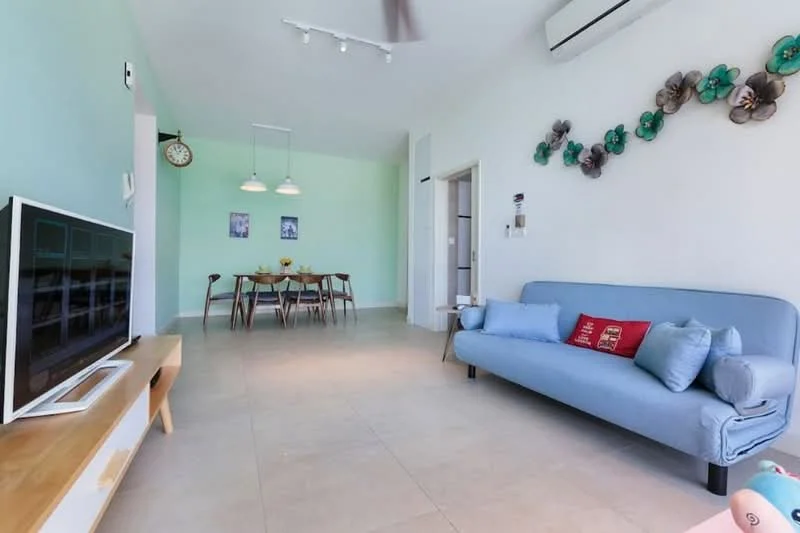 Living features: light blue fabric sofa, decorative cushions, wall-mounted TV, wooden TV console, recessed downlights, ceiling fan, cream tiled flooring, green accent wall, decorative wall flowers, open layout to dining area; style: modern. Dining features: wooden dining table, 4 wooden dining chairs, pendant lighting above table, green accent wall, cream tiled flooring; style: modern.