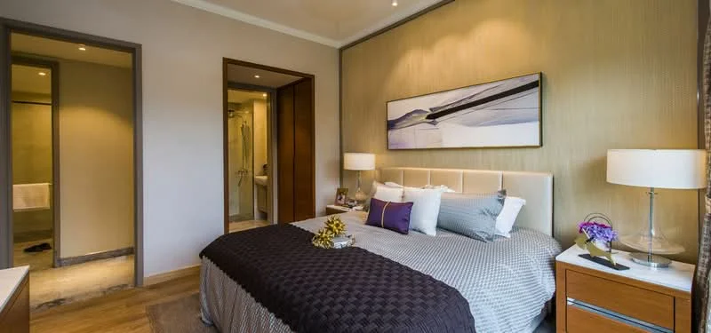Bedroom features: king-size bed with upholstered headboard, grey bedding with decorative pillows, nightstands with lamps, framed artwork on wall, wooden flooring, wall-mounted light fixtures, textured accent wall, built-in wardrobe with sliding doors, en-suite bathroom visible through door; style: modern.