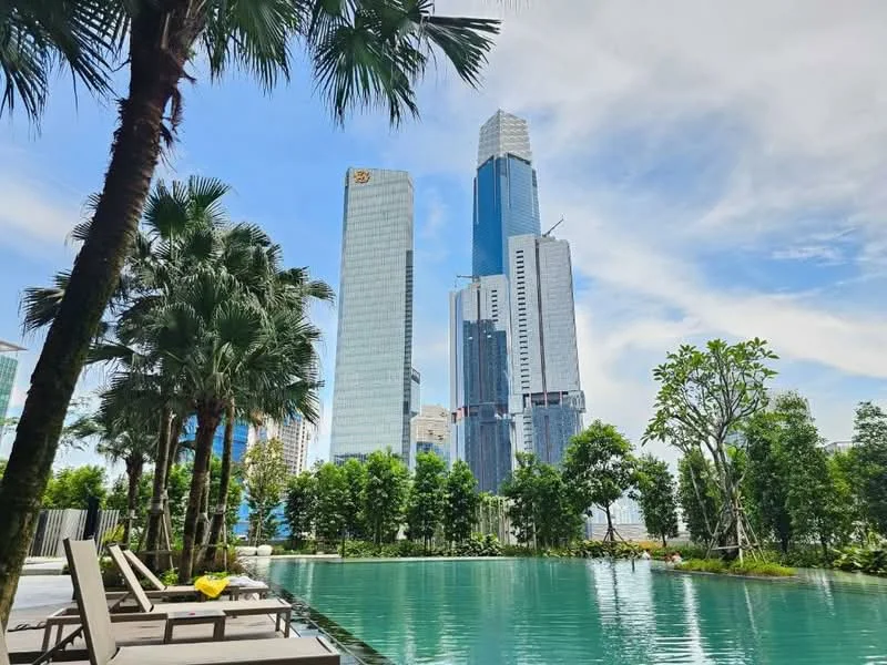 Exterior type: high-rise condominium; features: infinity pool, pool deck with loungers, surrounded by palm trees, manicured landscaping, city skyline view, modern glass facade buildings, lush greenery, urban setting; style: modern.