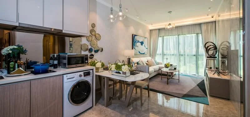 Kitchen features: white cabinetry, marble countertop, built-in microwave, stainless-steel washing machine, ceramic tile flooring; style: modern. Living features: 3-seater fabric sofa in light grey, coffee table with marble top, decorative wall art, area rug with geometric pattern, floor-to-ceiling windows with sheer curtains, pendant lighting, decorative sculptures, greenery in ceramic pots; style: modern; view: garden.