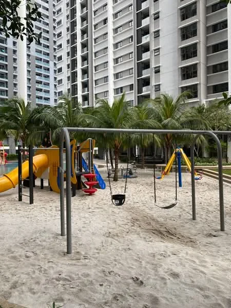 Exterior type: high-rise condominium; features: children's playground, swing set with two swings, slide, play structure with climbing features, sand surface, surrounded by palm trees, landscaped garden area, residential building facade in background; style: modern.