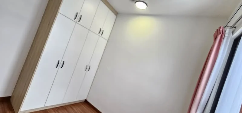 Bedroom features: built-in wardrobe with white doors, wooden flooring, recessed ceiling light, curtains with pink accents, window with sheer curtains, plain white walls; style: modern.