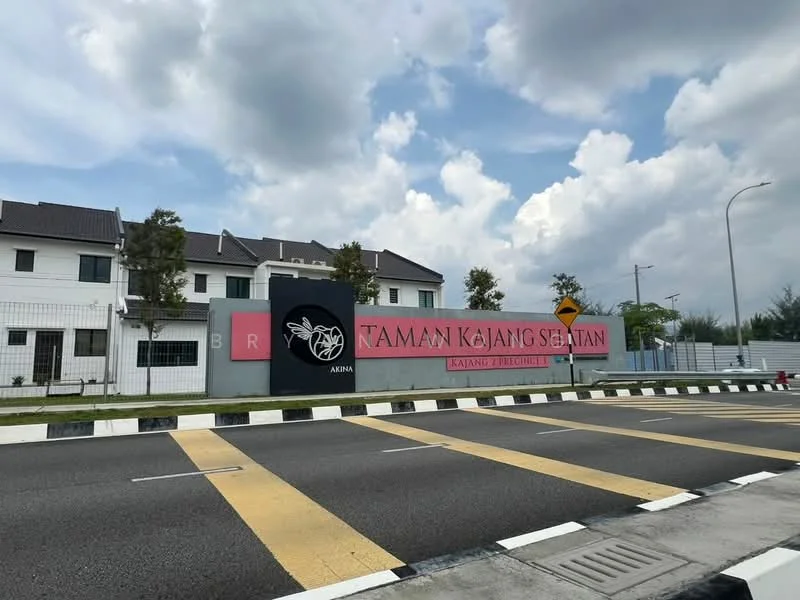 Exterior type: linked terrace house; features: signage with 'Taman Kajang Sejati', two-storey building, white painted facade, grey roof, manicured landscaping, surrounding fence, roadside view, traffic signage, pavement markings; style: modern.