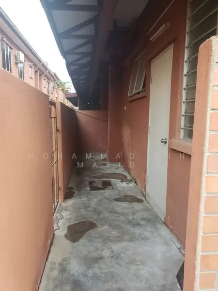Room features: concrete flooring, brown painted walls, metal door, small window, overhead roof with beams, narrow corridor.