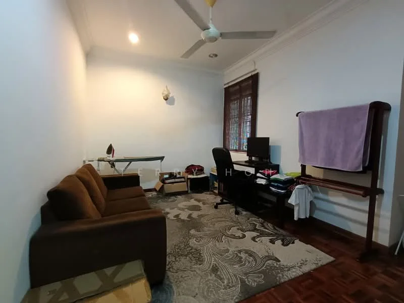 Living features: brown fabric sofa, wooden coffee table, area rug with floral pattern, ceiling fan, wall-mounted light fixture, window with wooden frame, computer desk with chair, ironing board, folding clothes rack, wooden flooring.