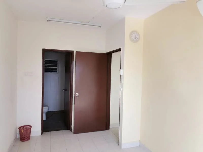 Room features: cream painted walls, white tiled flooring, single ceiling light fixture, wall clock, brown wooden door, doorway leading to bathroom, wastebasket, open space layout.