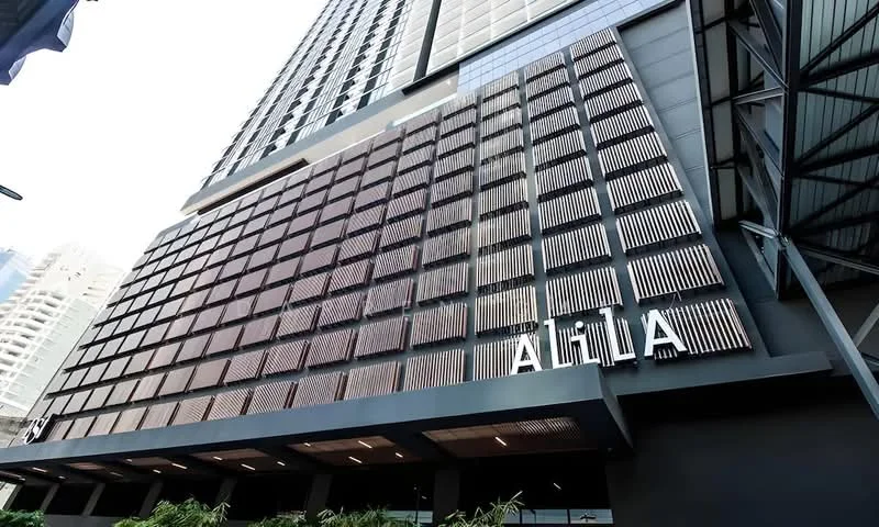 Exterior type: high-rise condominium; features: glass curtain wall, exposed concrete facade, horizontal louvre screens, projecting balconies, feature lighting at night, signage with the name 'ALIA', manicured landscaping at base; style: modern.