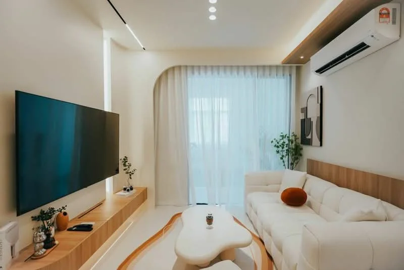 Living features: white leather sofa, wooden coffee table, wall-mounted TV, light wood feature wall, recessed downlights, floor-to-ceiling windows, sheer curtains, air conditioning unit, decorative plants, abstract wall art; style: modern.