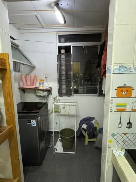 Kitchen features: grey tiled flooring, white walls, single-bowl stainless-steel sink, chrome pull-down faucet, black freestanding washing machine, white drying rack, window with blinds, kitchen cabinets, stove with exhaust hood, clothes drying area, green plastic bucket, blue cloth on the floor.