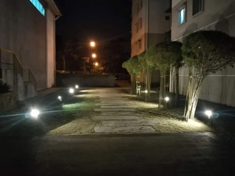 Exterior features: landscaped pathway, stepping stone walkway, outdoor lighting, manicured grass, trees along pathway, nighttime illumination; style: modern.