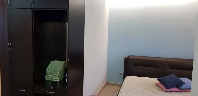 Bedroom features: queen-size bed, upholstered headboard, built-in wardrobe with sliding doors, light blue painted walls, cream tiled flooring, decorative pillows on bed, small bedside table, window with natural light; style: modern.