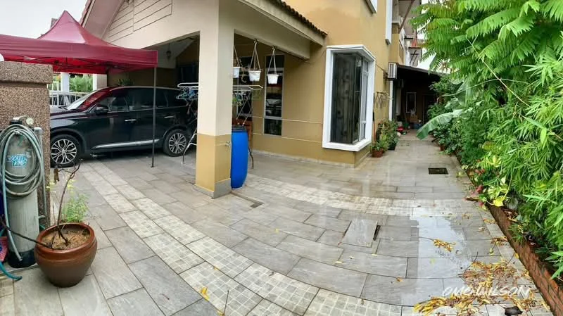 Exterior type: linked terrace house; features: paved walkway, car parked in driveway, garden area with plants, water barrel, clothes drying rack, covered area with tent, decorative pot, exterior wall with beige paint, large window, greenery along the side; style: modern.