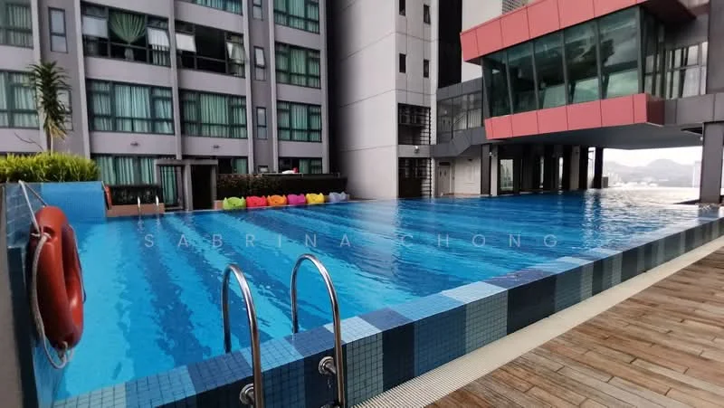 Exterior type: high-rise condominium; features: infinity pool, pool deck with loungers, glass curtain wall, red accent facade, wooden decking around pool, landscaped area with plants, safety buoy, city skyline view in background; style: modern.