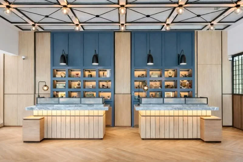 Room features: wood paneling on walls, blue accent wall, marble countertop, wooden cabinetry, suspended pendant lights, recessed lighting, display shelves with decorative items, herringbone wood flooring, exposed ceiling beams, glass partition, ambient lighting under cabinetry; style: modern.