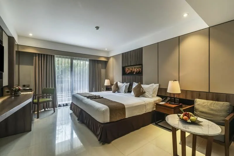 Bedroom features: king-size bed with brown and white bedding, upholstered headboard, two bedside lamps, wooden bedside table, marble flooring, large window with sheer curtains, green accent chair, decorative wall art, wall-mounted TV, wooden feature wall, small round table with fruit bowl; style: modern; view: garden.