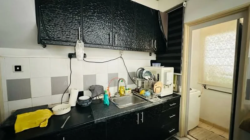 Kitchen features: black laminate cabinetry, stainless-steel sink, chrome faucet, black countertop, white tiled backsplash, dish rack, kitchen utensils, cleaning supplies, white appliances, washing machine, window with sheer curtains; style: modern.