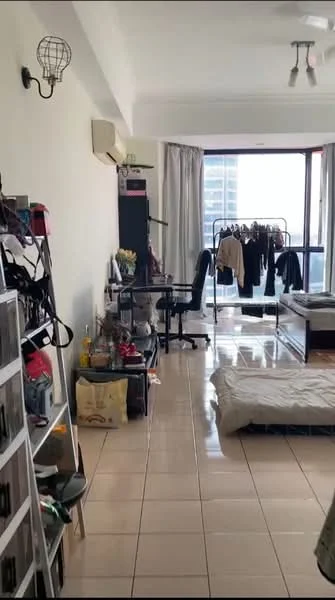 Living features: cream painted walls, glossy tile flooring, floor-to-ceiling windows, sheer curtains, ceiling fan, wall-mounted air conditioning unit, clothes rack, black desk, bed with bedding, shelving unit, decorative plants, various storage boxes; style: modern; view: city.