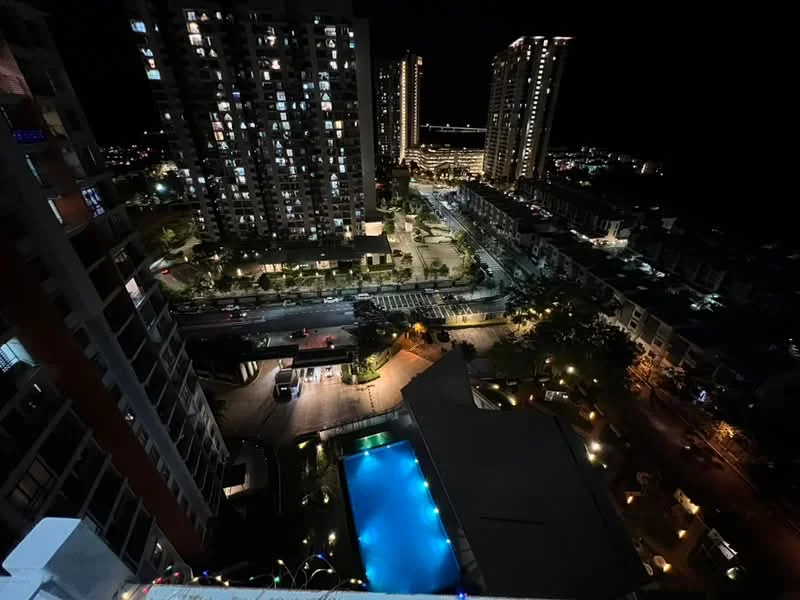 Exterior type: high-rise condominium; features: night view of city skyline, swimming pool with illuminated edges, surrounding high-rise buildings, landscaped areas with lighting, street view with vehicles, outdoor amenities visible, well-lit pathways, multiple floors of residential units; style: modern.