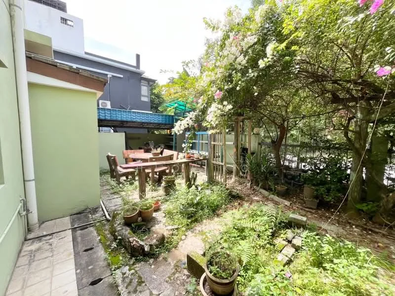 Exterior features: garden area, wooden dining table, potted plants, stone pathway, lush greenery, fenced area, outdoor seating, canopy cover, flowering plants; style: tropical-modern.