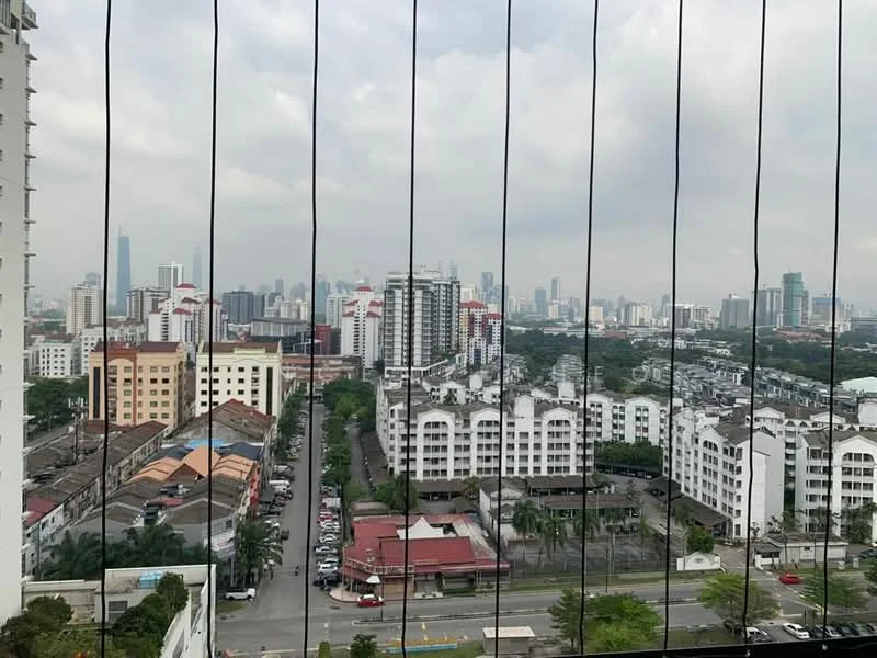 Exterior type: high-rise condominium; features: city skyline view, glass balcony railing, surrounding residential buildings, urban landscape, visible road with parked cars, greenery in the foreground; style: modern.