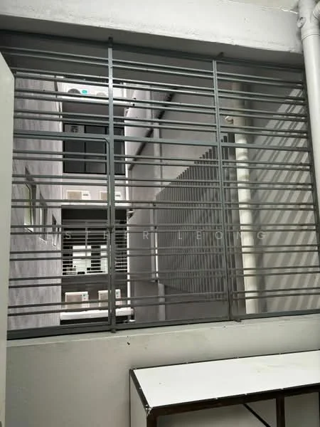 Room features: metal window grilles, concrete walls, white painted walls, table, narrow view of adjacent building, vertical metal bars.