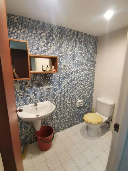 Bathroom features: white pedestal sink, chrome faucet, yellow toilet seat, one-piece toilet, mosaic tile wall in blue and white, white tiled flooring, wooden wall-mounted shelf, mirror above sink, lighting fixtures in ceiling; style: modern.