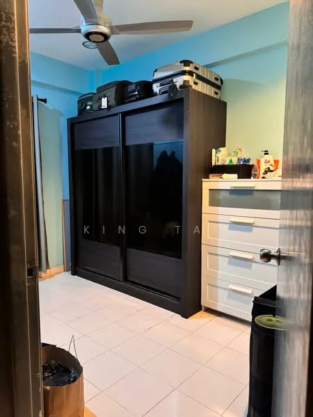Room features: black sliding wardrobe, white chest of drawers, ceiling fan, light blue painted walls, white tiled flooring, suitcases on top of wardrobe, various items on chest of drawers, curtain on window, black storage unit.