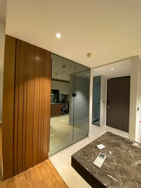 Room features: wood paneling on wall, glass partition, marble flooring, recessed lighting, open layout, kitchen area visible, dark wood door, light grey walls; style: modern.