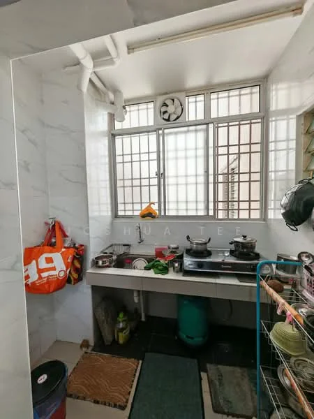 Kitchen features: white marble wall cladding, grey tiled flooring, double-burner gas stove, stainless-steel cooking pots, wall-mounted exhaust fan, window with metal grille, sink with faucet, open shelving, green gas cylinder, kitchen mats, plastic storage rack, hanging utensils; style: functional.