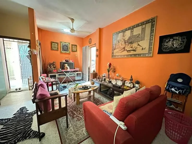 Living features: orange painted walls, ceiling fan, 3-seater fabric sofa in red, wooden armchair, coffee table, area rug with geometric pattern, TV console, decorative wall art, framed artwork, shelves with decorative items, curtains, tile flooring; style: traditional. Room features: doorway leading to outdoor area, decorative plants.