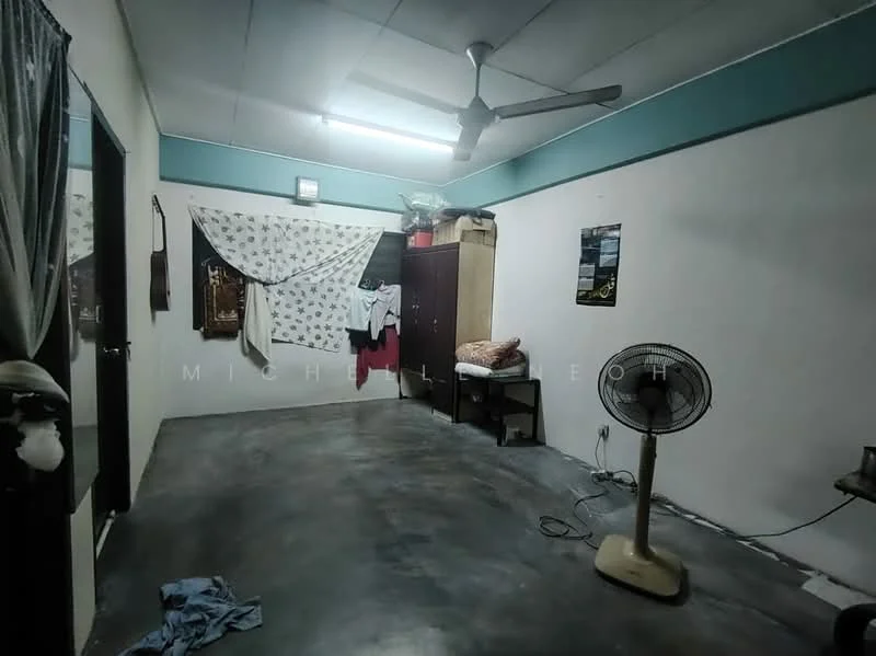 Room features: grey polished concrete flooring, white painted walls, ceiling fan, wall-mounted light fixture, wooden wardrobe, decorative wall hanging, freestanding pedestal fan, window with curtain, clothes hanging on wall; style: minimalist.