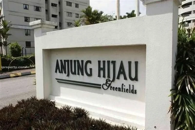 Exterior features: signage with name 'ANJUNG HIJAU & greenfields', white painted facade, landscaped garden with plants, paved driveway, surrounding residential buildings; style: modern.