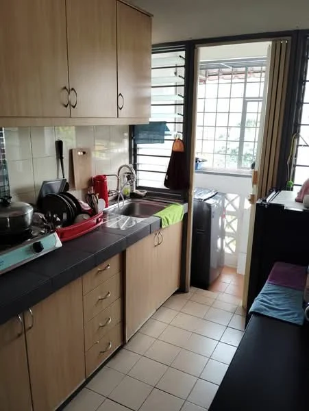 Kitchen features: wood cabinetry in light brown, black countertop, single-bowl stainless-steel sink, chrome pull-down faucet, built-in stove with gas burners, dish rack, kitchen utensils, window with metal grills, tile flooring in white, open doorway leading to balcony, green dishcloth, red kettle; style: modern.