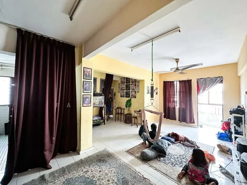 Living features: cream painted walls, white ceiling, ceiling fan, floor tiles, large windows with curtains, hammock, area rug with geometric pattern, wall-mounted artwork, decorative wall frames, seating cushions on the floor, cluttered storage items, dark curtains, open layout; style: casual. Kitchen features: white walls, tile flooring, open layout to living area, visible kitchen items, dark curtains.