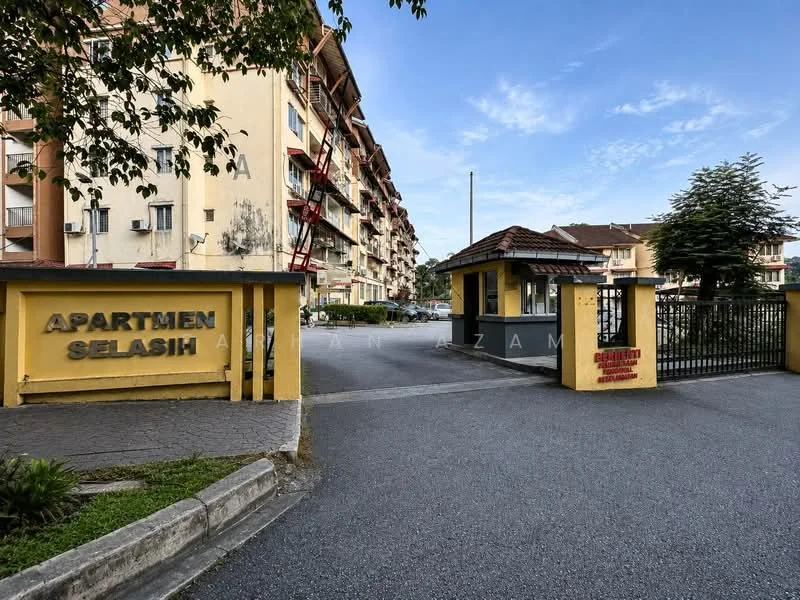 Exterior type: low-rise apartment block; features: yellow painted facade, guard house at entrance, paved driveway, landscaped greenery, multiple storeys, balconies with railings, surrounded by trees, signage at entrance; style: modern.