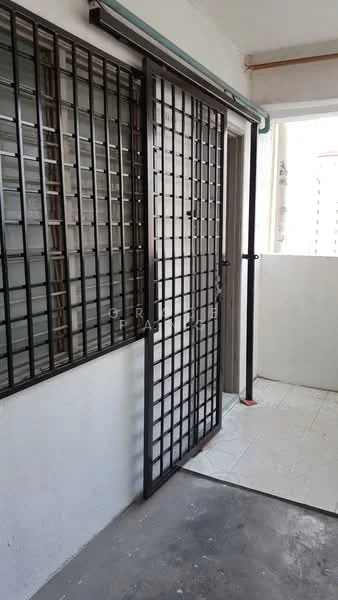 Room features: metal security grille door, white painted walls, grey concrete flooring, window with metal grilles, light coming from outside.