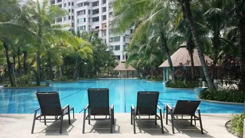 Exterior type: swimming pool deck; features: infinity pool, pool deck with loungers, tropical landscaping, palm trees, thatched-roof gazebo, manicured lawn, surrounded by greenery; style: tropical-modern.