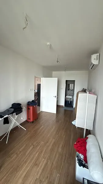 Room features: light wood laminate flooring, white painted walls, 1 wall-mounted split AC, 2 ceiling lights, folding ironing board, white storage cabinet, red and black clothing on sofa, orange suitcase, door leading to another room; style: modern.