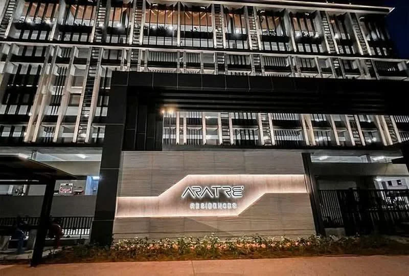 Exterior type: low-rise apartment block; features: glass curtain wall, black painted facade, illuminated signage, manicured landscaping, modern architectural design, multiple balconies, feature lighting at night; style: modern.