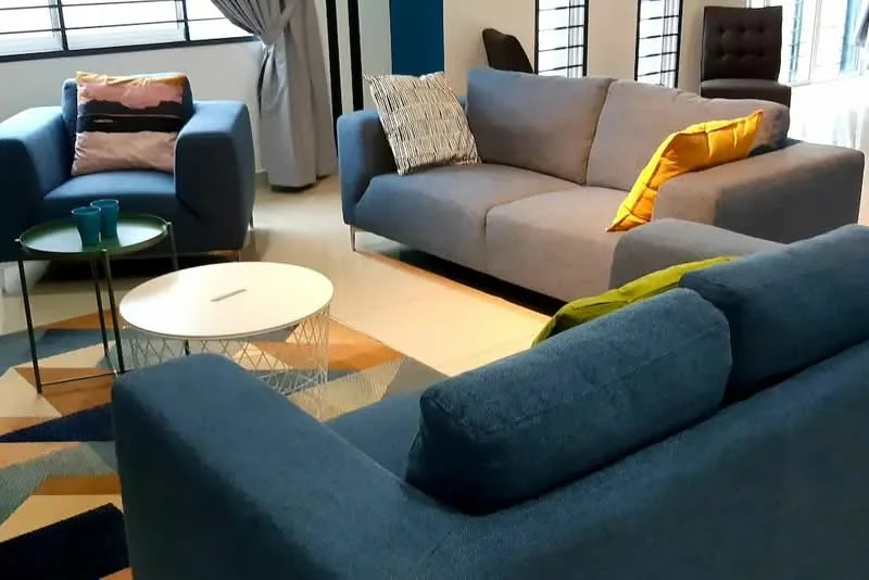 Living features: 3-seater fabric sofa in blue, 2-seater fabric sofa in blue, yellow accent cushion, grey accent cushion, round coffee table with metal base, area rug with geometric pattern, floor-to-ceiling windows, curtains, decorative wall with blue paint, wall-mounted artwork; style: modern.
