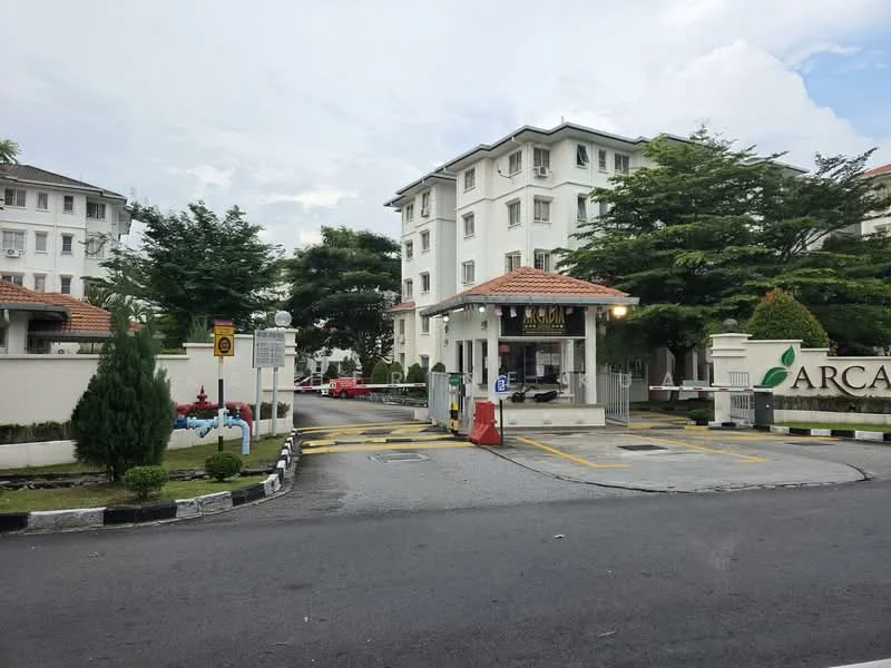 Exterior type: gated community; features: white painted facade, flat roof with terracotta tiles, 3-storey low-rise, manicured lawn, mature trees, guard house at entrance, boom gate, CCTV cameras visible, gated entry, paved driveway, landscape garden, signage at entrance; style: modern.