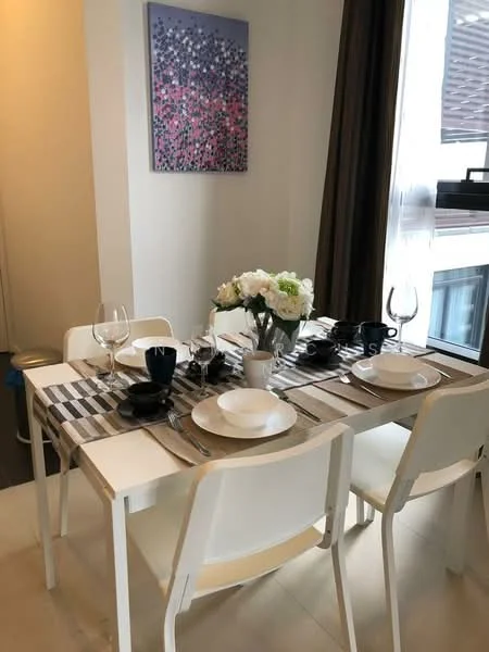 Dining features: dining table with white surface, 4 white dining chairs, black dinner plates, white bowls, wine glasses, cutlery set, table runner with striped pattern, floral centerpiece, large window with sheer curtains, wall art with abstract design, light-colored walls, tile flooring; style: modern.